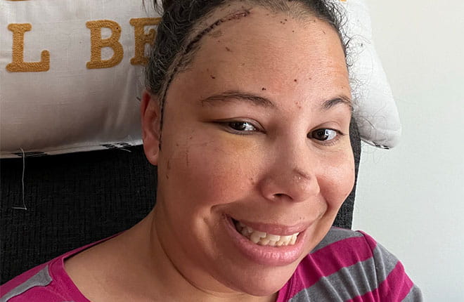 Darnetta Yusko in a pink striped shirt sitting in front of a cushion with letters.