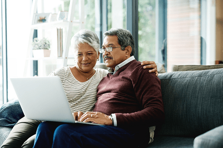 Older couple sitting on a couch, researching on a laptop.