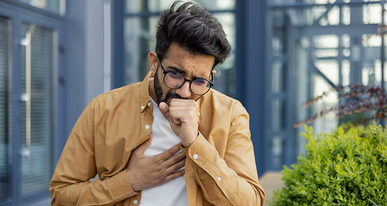 A man stands outside a building coughing