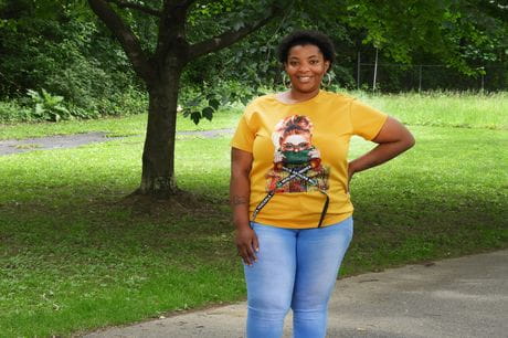 Kareba Lee standing outside, smiling with her hand on her hip.