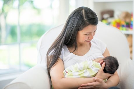 A mother sitting in a chair, breastfeeding her newborn baby.