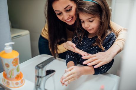 Happy woman with her young daughter, washing their hands to protect themselves from coronavirus and other illnesses.