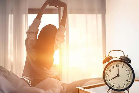 A woman wakes to a sunrise through her bedroom windows.