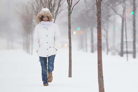 A woman walks alone on a city sidewalk in the snow.