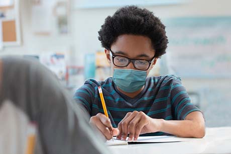Child with glasses in class with a blue mask on