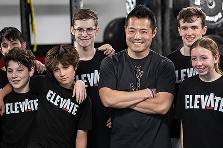 A man stands in the middle of a group of smiling teenagers.