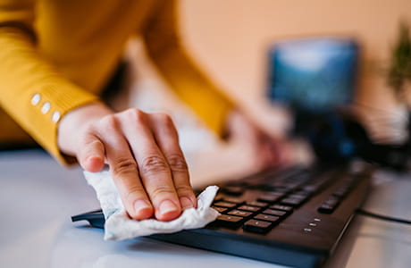 A woman cleaning / disinfecting a computer keyboard.