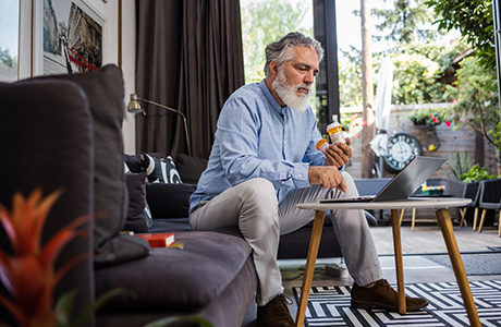 A man in his 50s is holding pill bottles while searching for information online