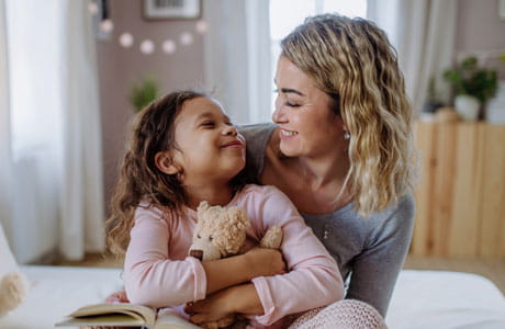 A daughter sitting on mothers lap smiling at one another. 