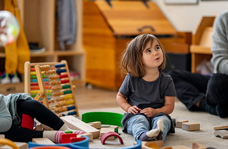 A toddler is seen playing on the floor at daycare with her friends.
