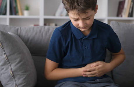 Young boy sitting on a couch, holding onto his stomach