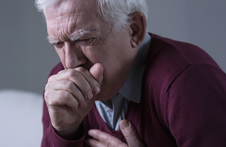 An elderly man in discomfort coughs into his hand.