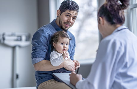 A father taking his daughter to see a pediatrician to discuss vaccines.