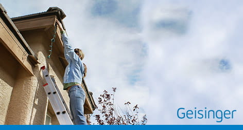 Person strectching - putting up holiday lights outdoors on a ladder