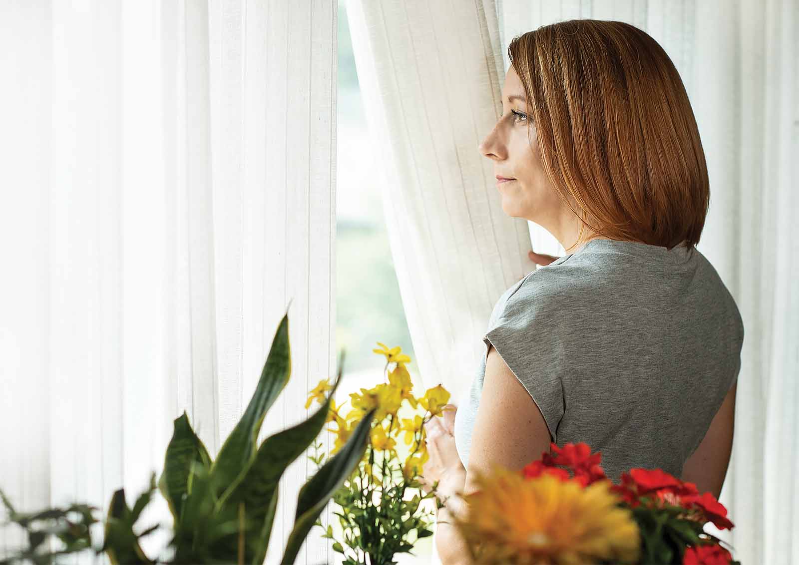 A woman gazes out the window prior to going outside to her garden.