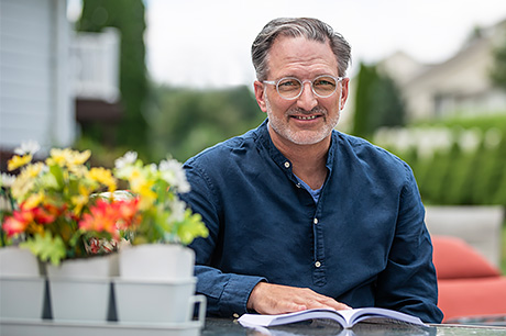 Man in a blue shirt reading at a table with a flower arrangement.