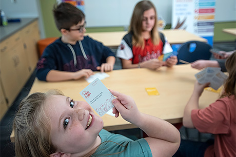 Students sitting at a table playing a card game in a classroom.
