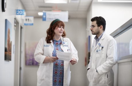 Two palliative medicine specialist talk in a hospital hallway.