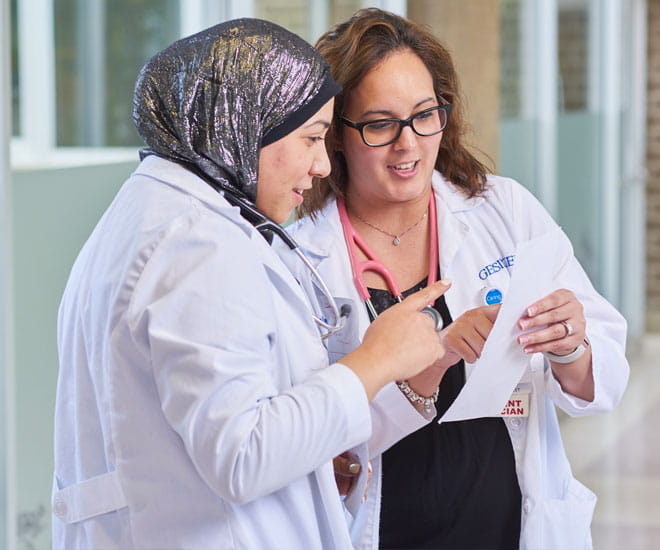 Two female hospital physicians conferring on notes.